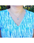 Person wearing a blue and white patterned top with a opal necklace outdoors.