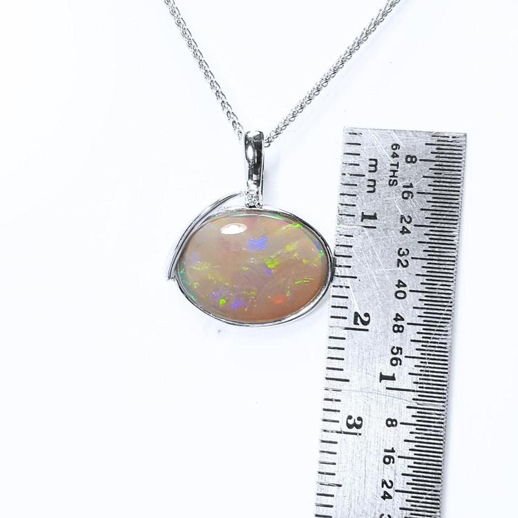 Opal pendant on a white gold chain with a ruler for scale on a white background