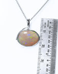 Opal pendant on a white gold chain with a ruler for scale on a white background