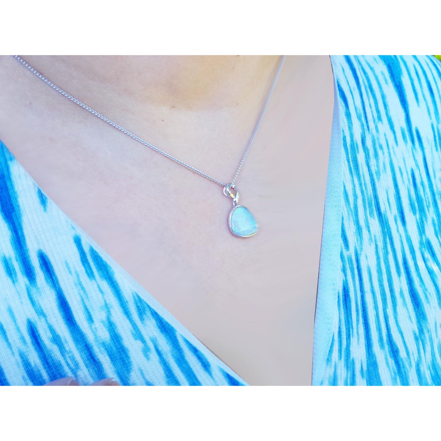 Teardrop-shaped opal pendant necklace worn by a person with a blue and white patterned garment.