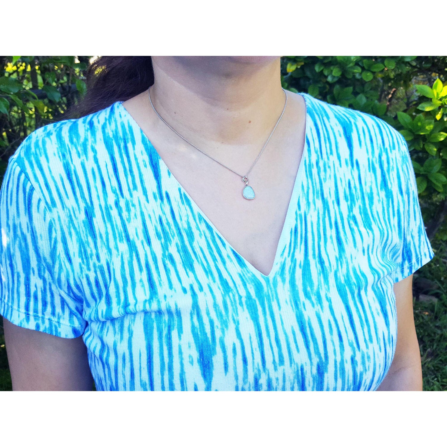 Person wearing a blue and white patterned top and opal pendant with a blurred green background.