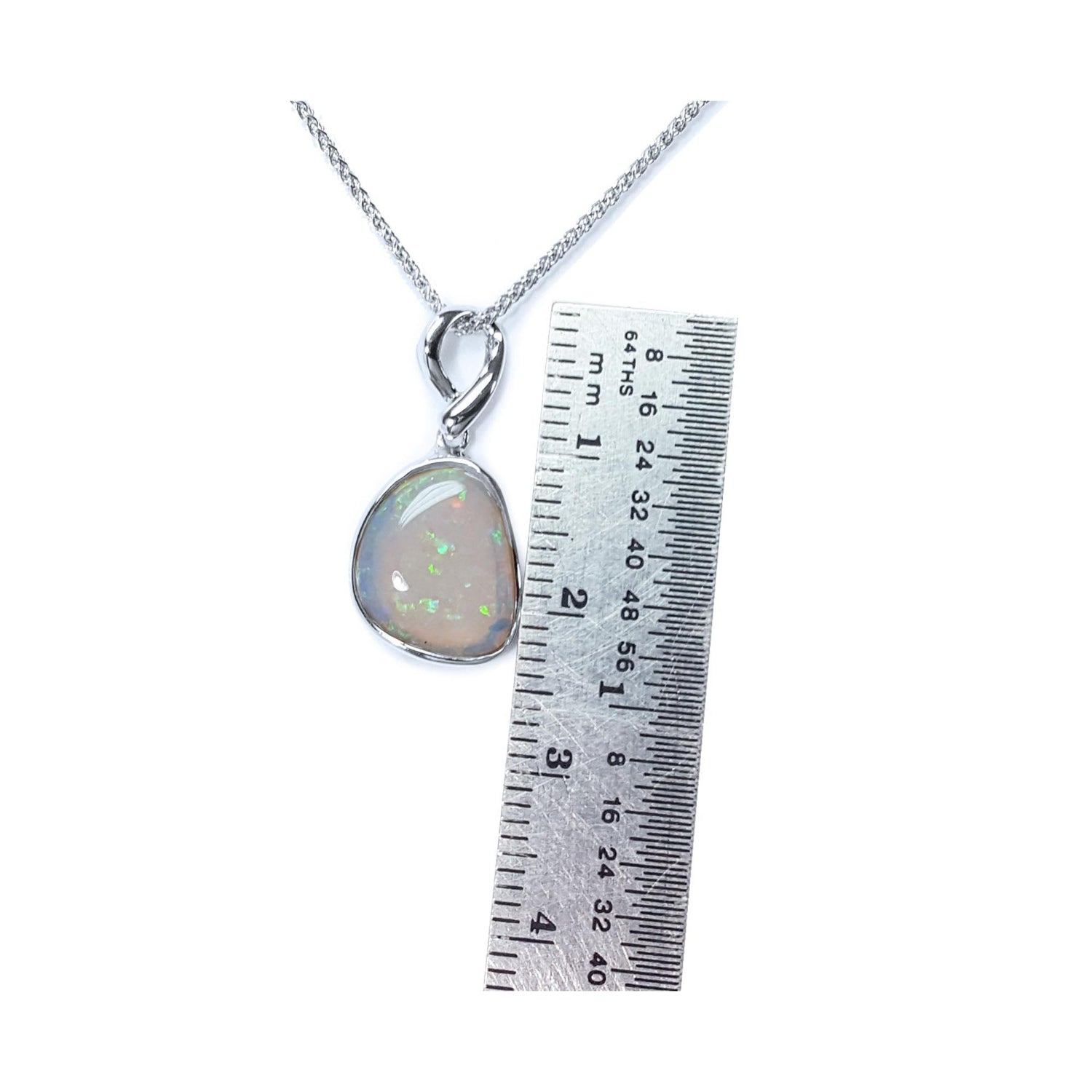 Opal pendant on a white gold chain with a ruler for scale on a white background