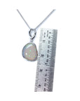 Opal pendant on a white gold chain with a ruler for scale on a white background