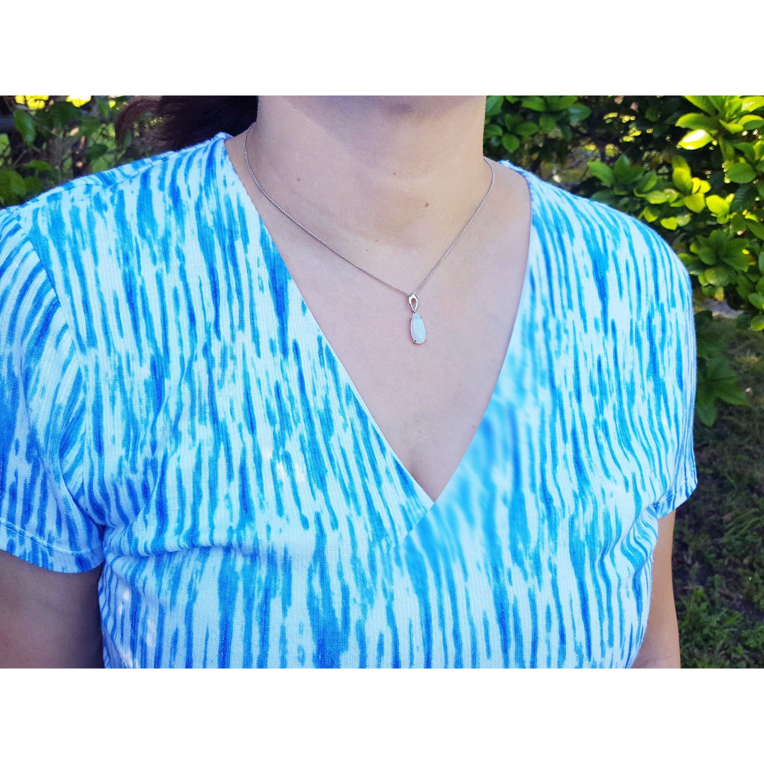 Person wearing a blue and white patterned dress with an opal necklace, standing outdoors.