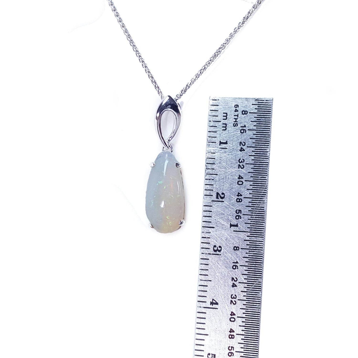 Necklace with an opal pendant next to a ruler on a white background