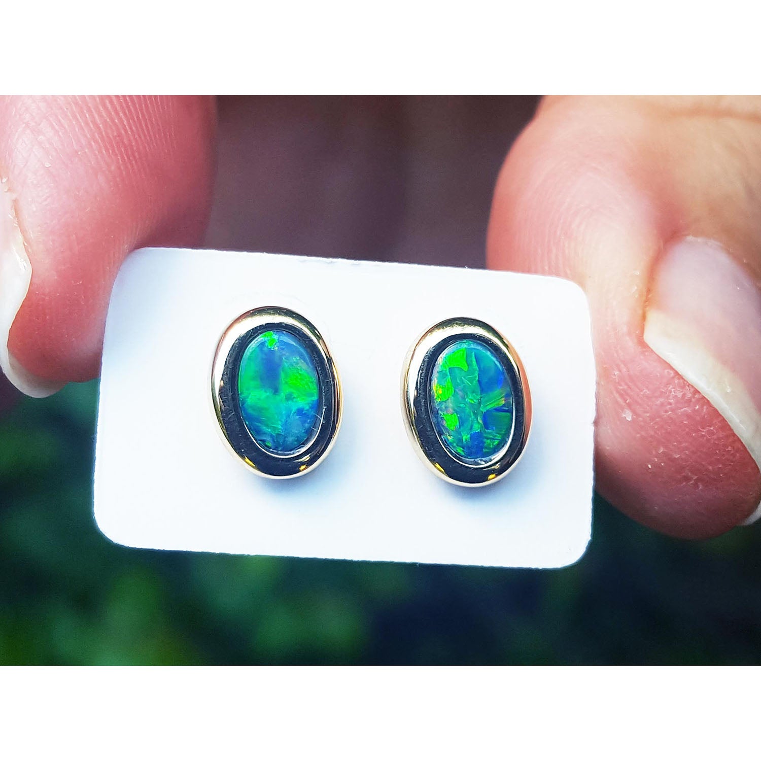 Opal earrings held on a white card between fingers.