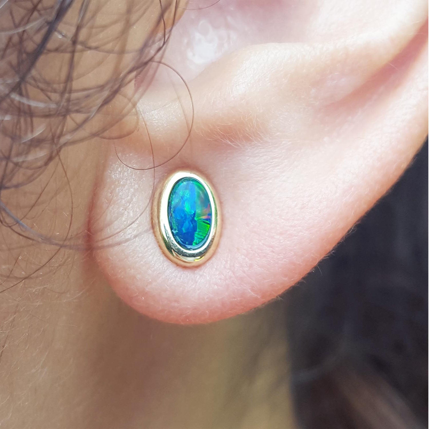 Close-up of an opal earring on a person's ear.