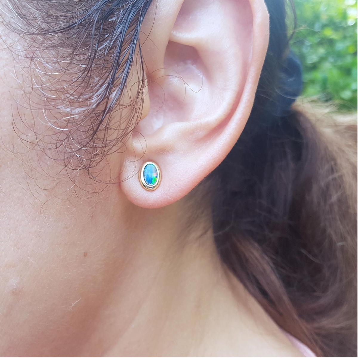 Close-up of an ear wearing a gold earring with an Australian opal, outdoors.