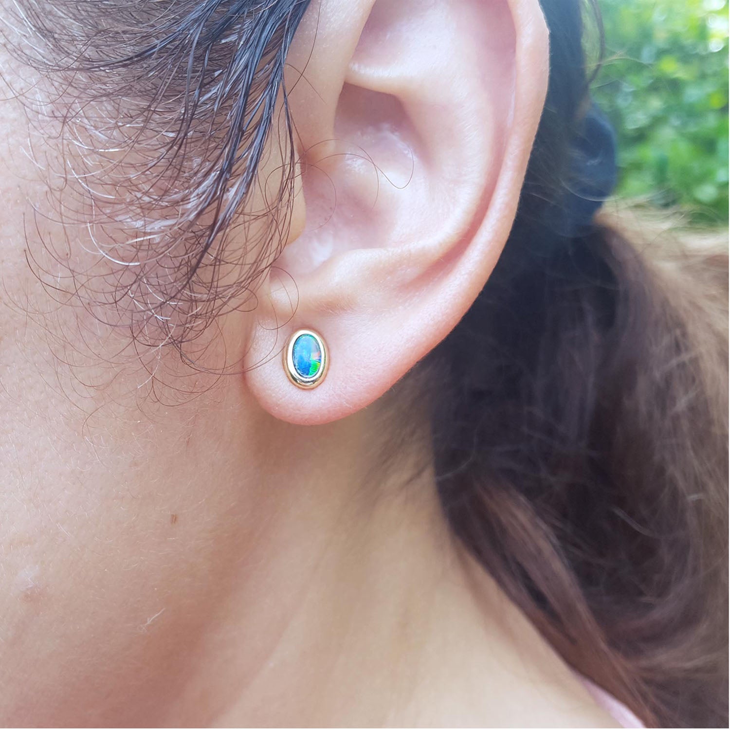 Close-up of an ear wearing a gold earring with an Australian opal, outdoors.