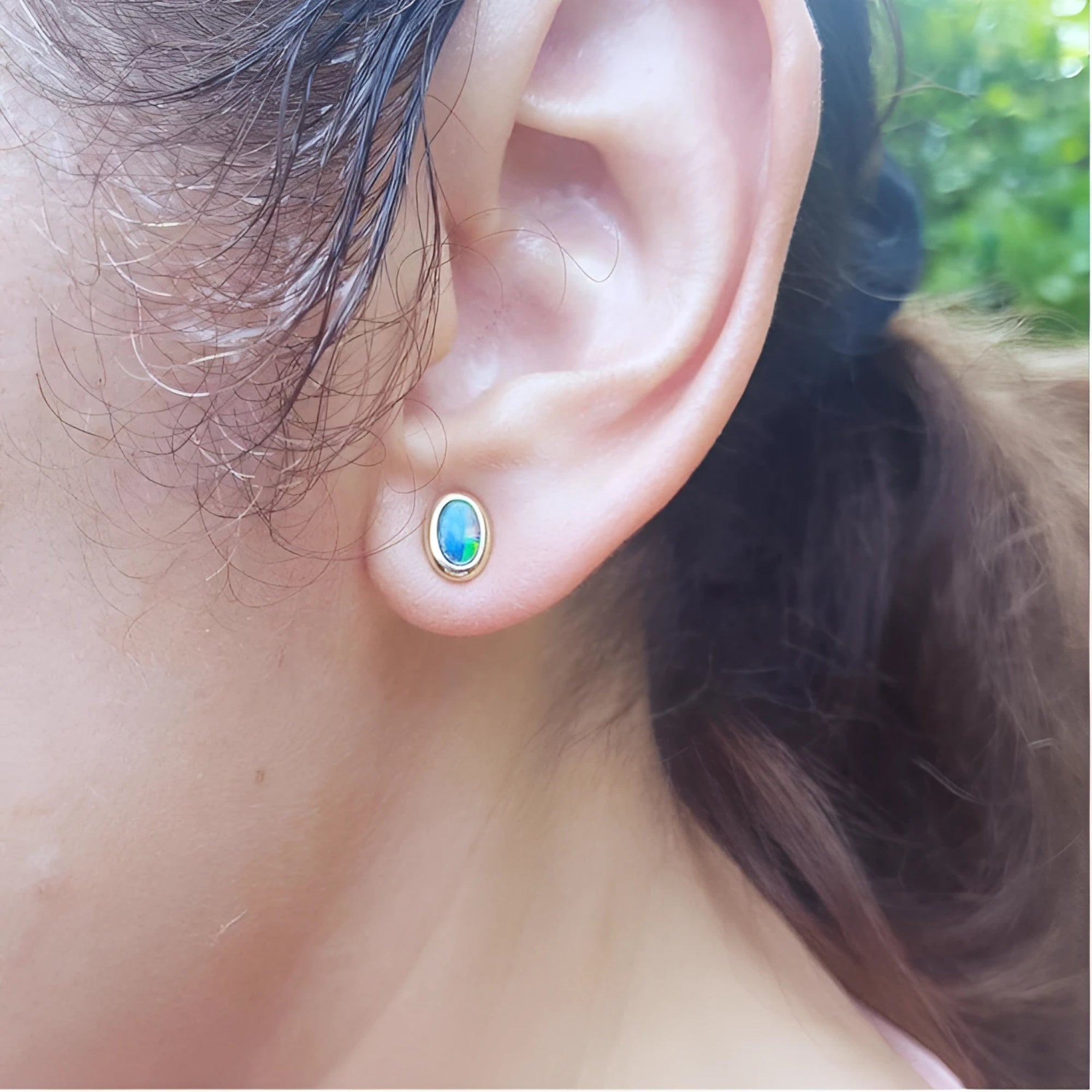 Oval blue Australian opal doublet stud earring in 14k yellow gold, bezel set on an ear.