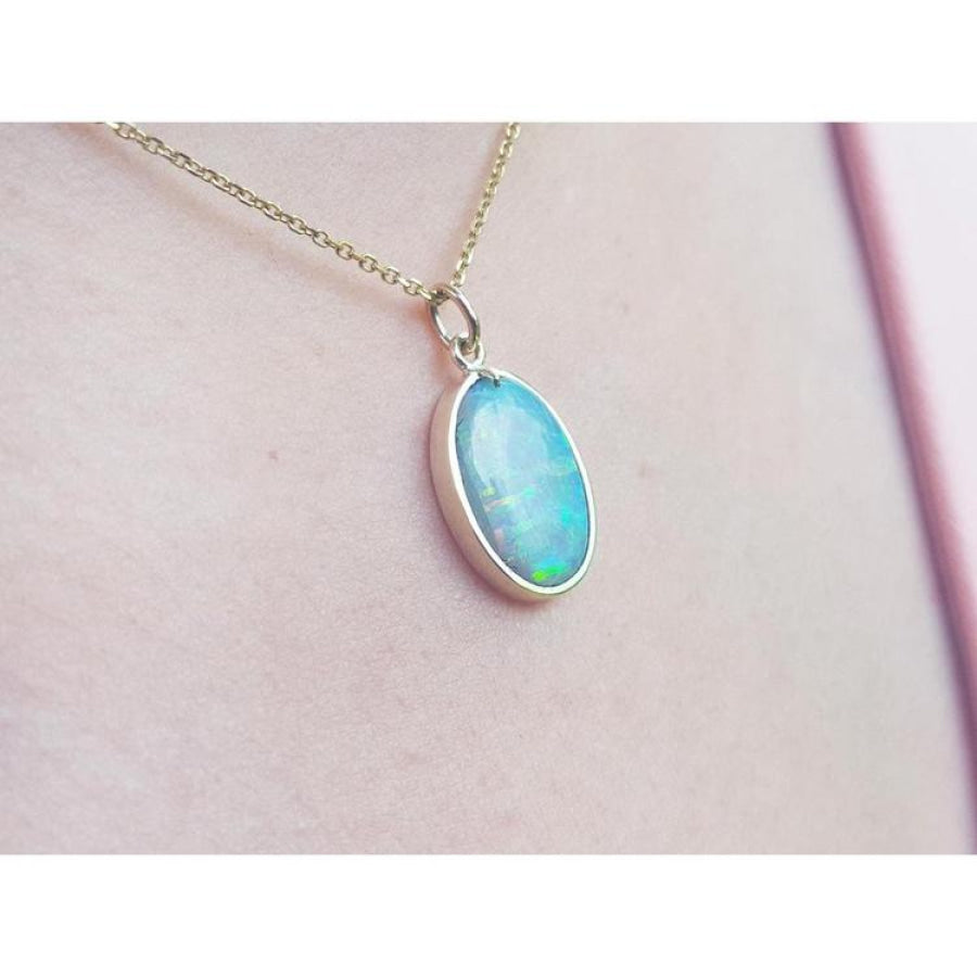 Oval Australian opal pendant with green-bluish hues in a 14K yellow gold setting on a chain.