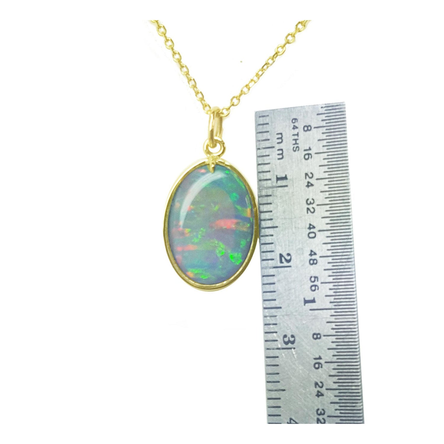 Opal pendant necklace with gold chain next to a ruler for scale on a white background
