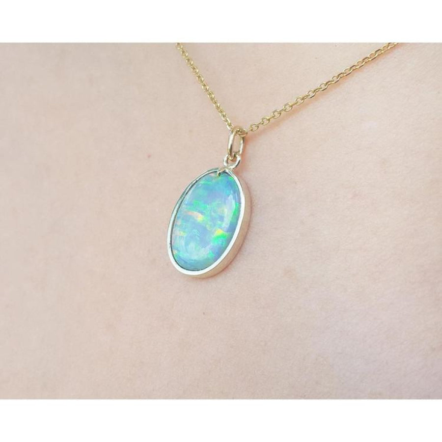 Oval Australian opal pendant with green-bluish rainbow play, set in 14K yellow gold on a chain.