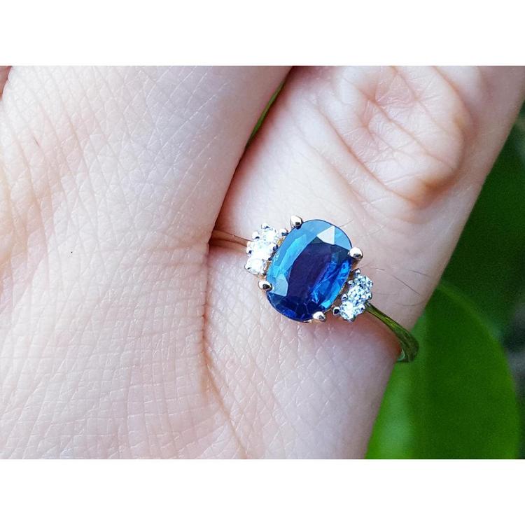 Blue sapphire ring with side diamonds on a hand against a blurred green background