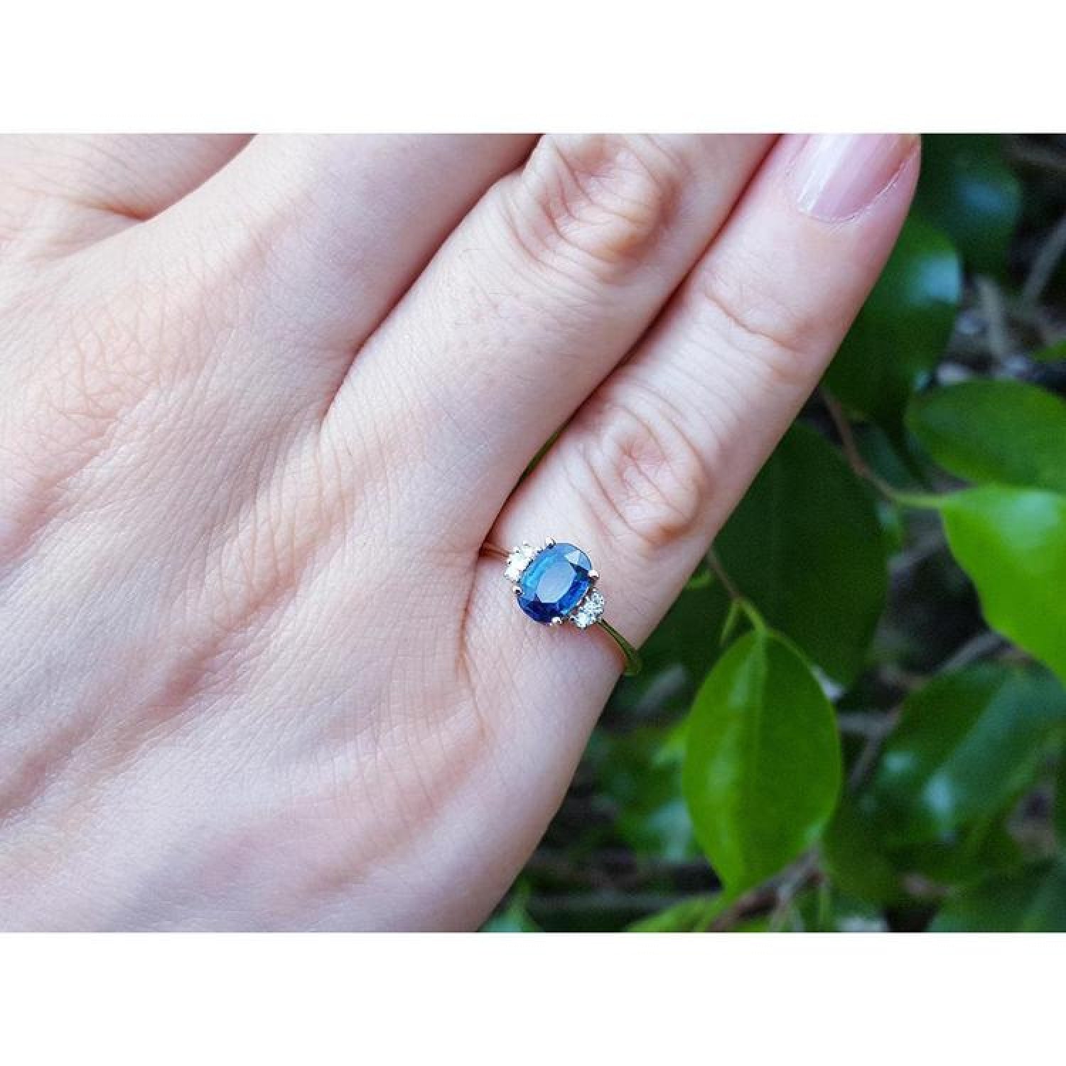 14K yellow gold ring with an oval blue sapphire and two natural diamonds on each side, worn on a finger.