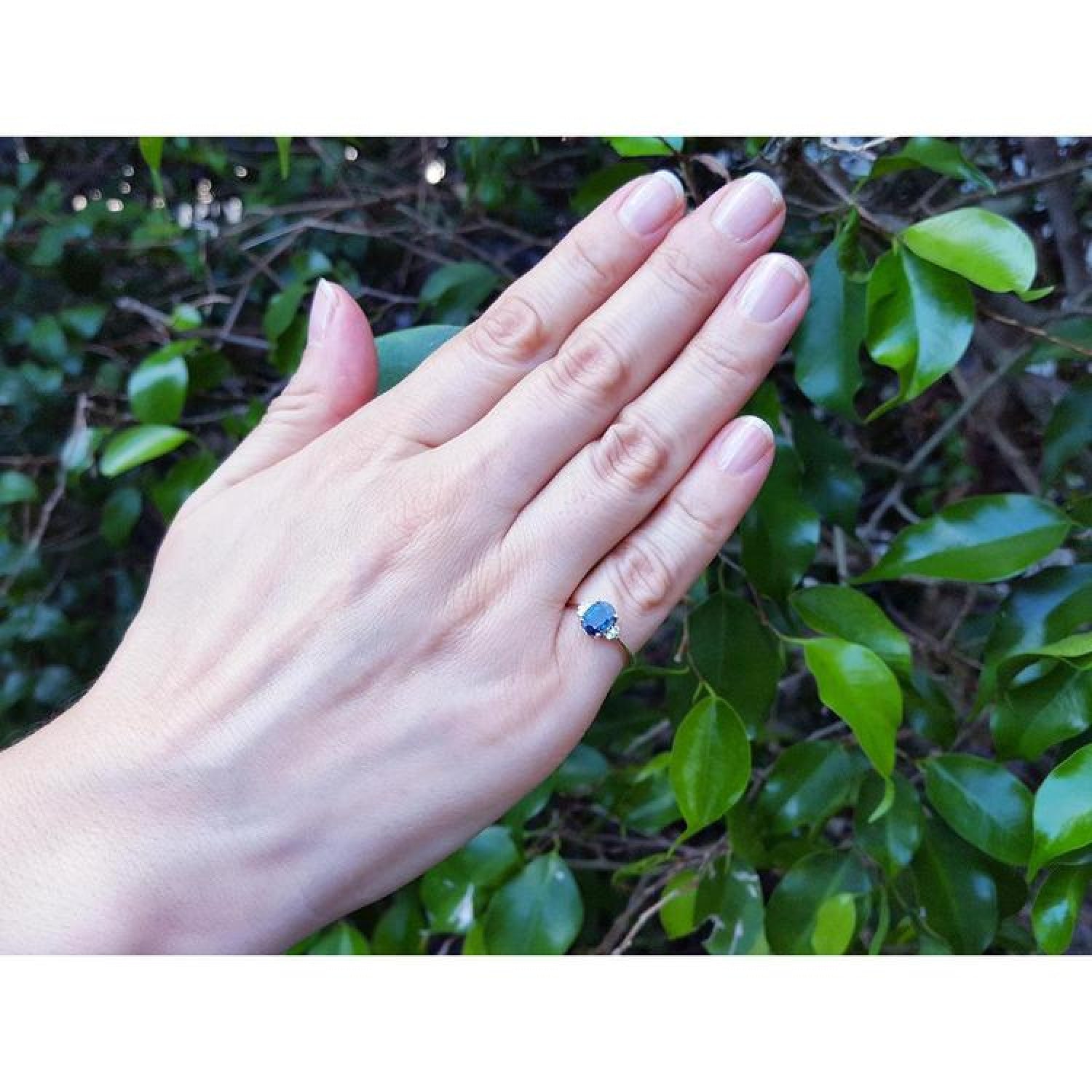 14K yellow gold ring with a vibrant oval blue sapphire and two natural diamonds on a hand.
