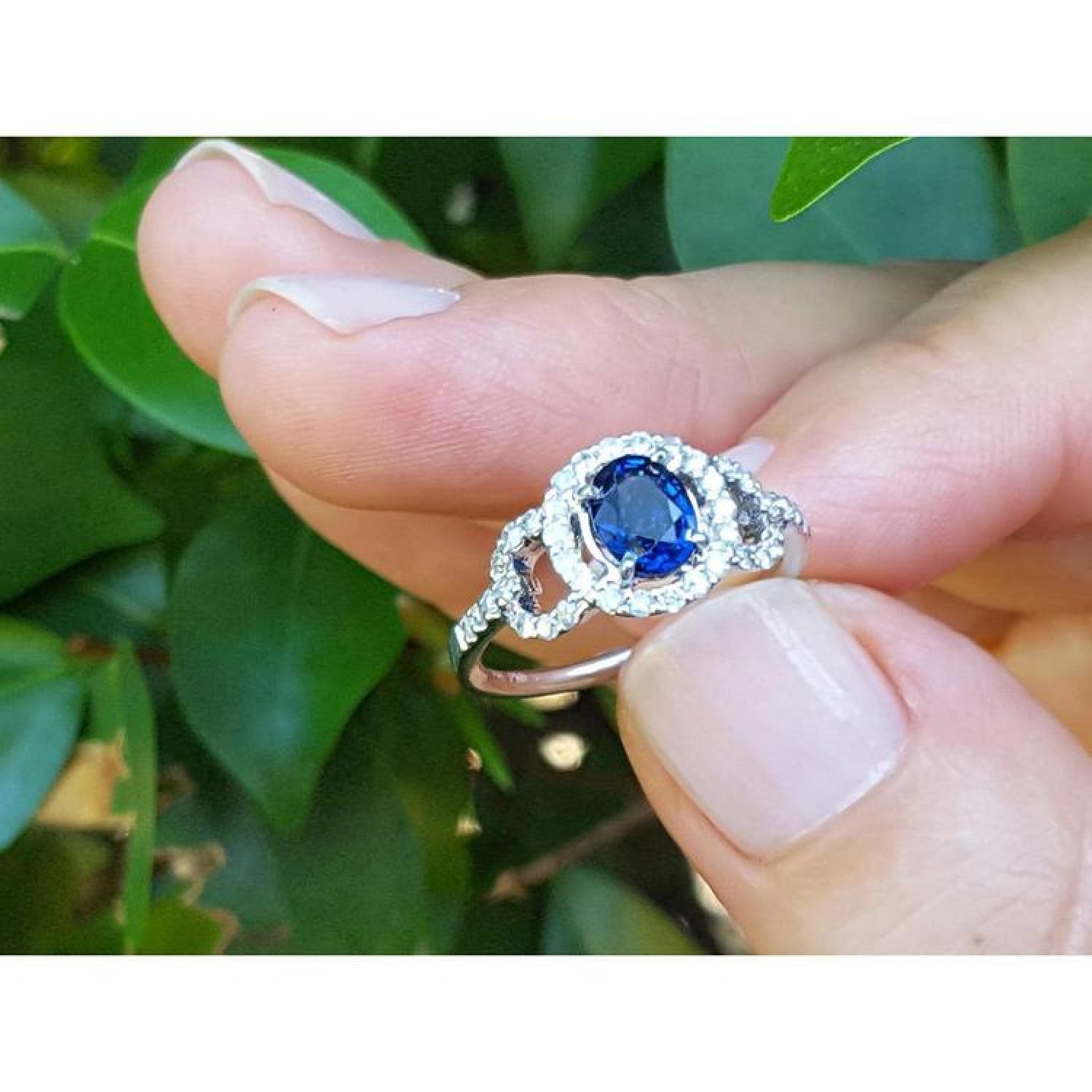1.08 ct oval blue sapphire ring in 14K white gold with diamond halo, held by fingers.