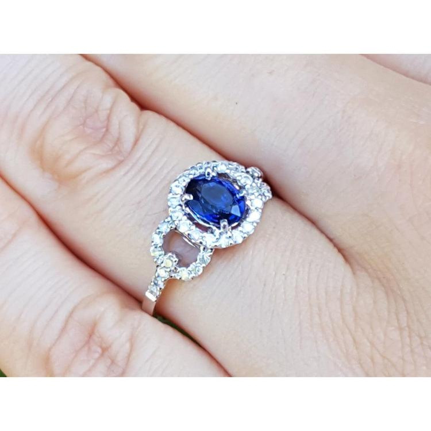1.08 ct oval blue sapphire ring with diamond halo and 14K white gold band on a finger.