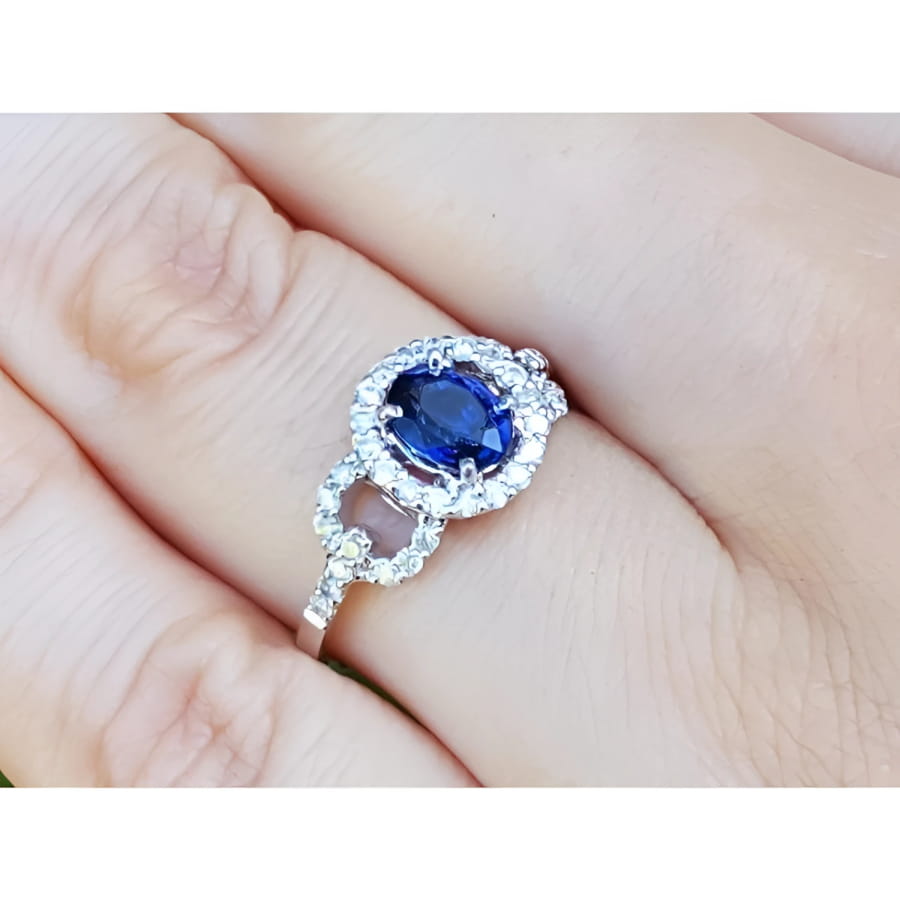 1.08 ct oval blue sapphire ring with diamond halo and 14K white gold band on a finger.