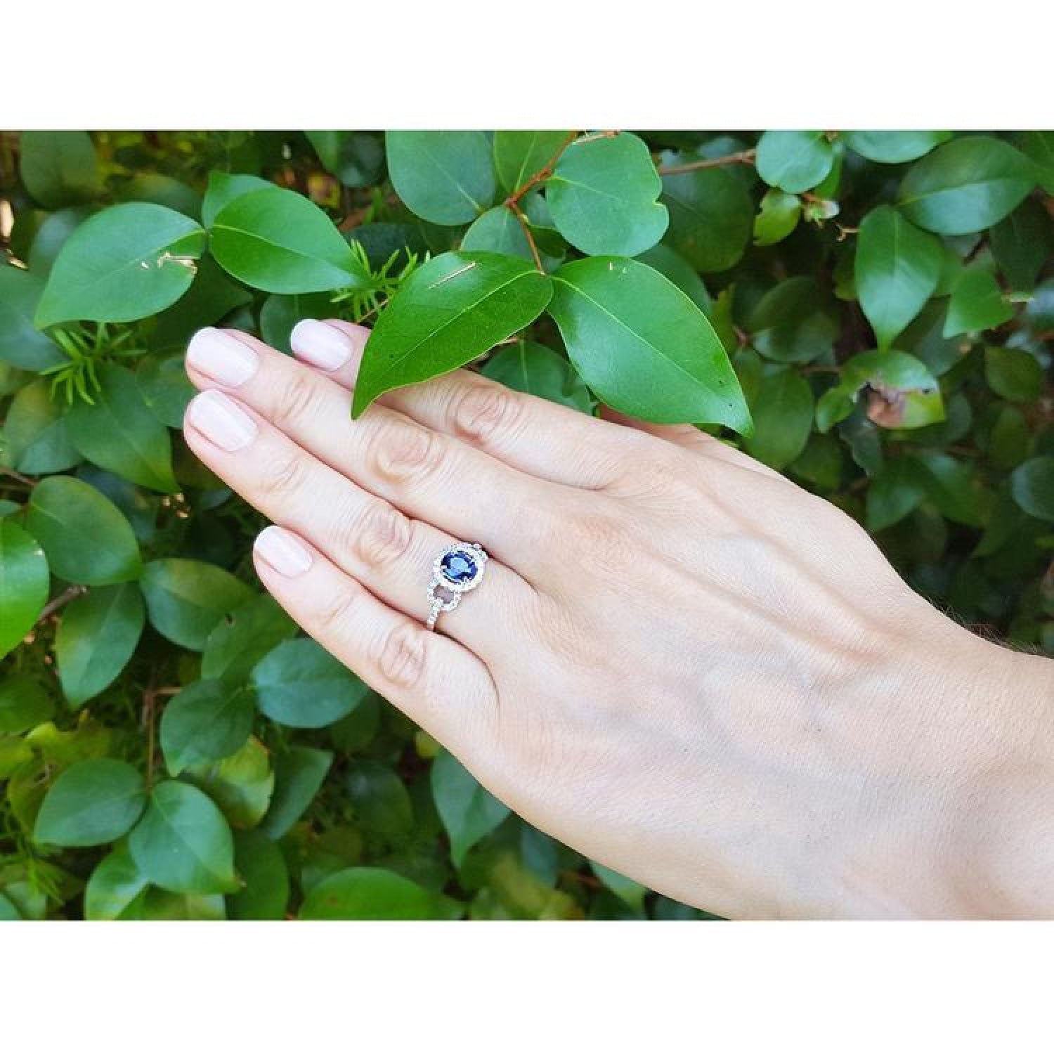 1.08 ct oval blue sapphire ring in 14K white gold with diamond halo on a hand.