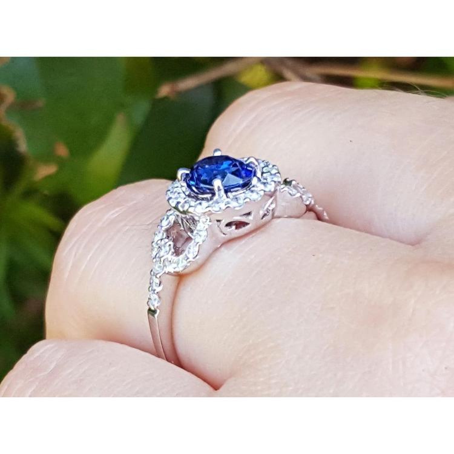 1.08 ct oval blue sapphire ring in 14K white gold with diamond halo on a finger.