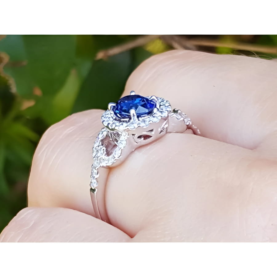 1.08 ct oval blue sapphire ring in 14K white gold with diamond halo on a finger.