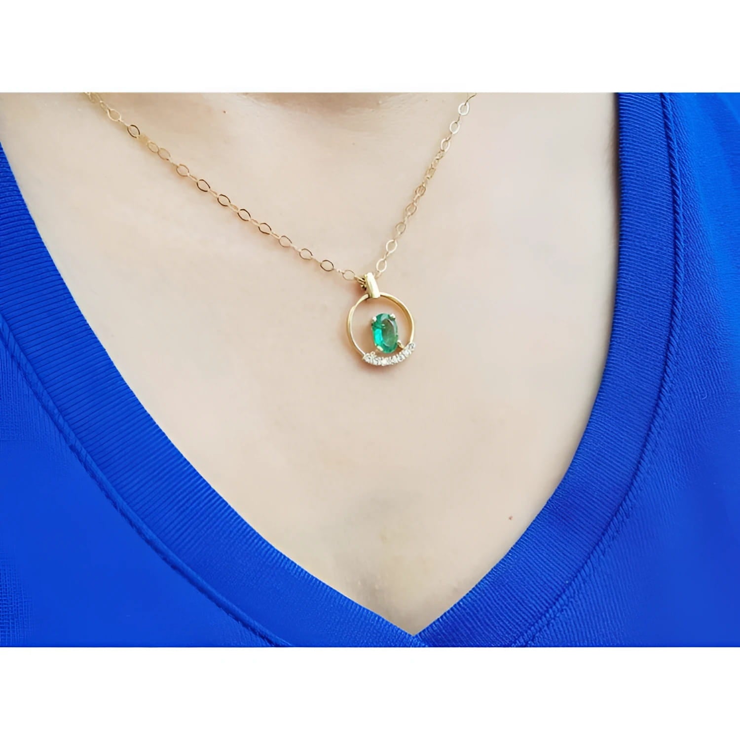 14k yellow gold necklace with an oval Colombian emerald and diamond pendant on a blue top.