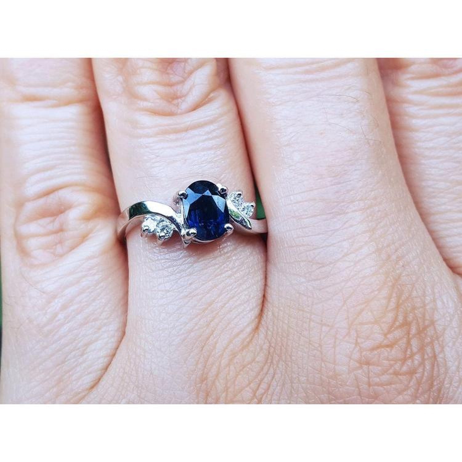 1.43 ct oval natural deep blue sapphire ring with accent diamonds set in 14K white gold on a hand.