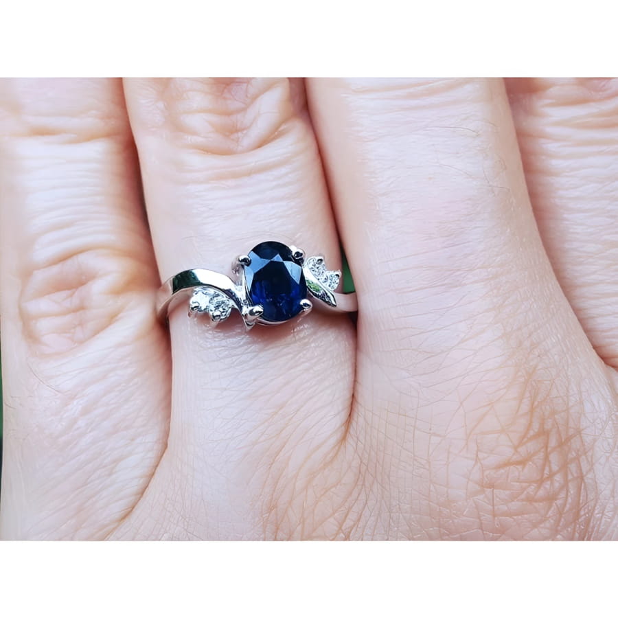 1.43 ct oval natural deep blue sapphire ring with accent diamonds set in 14K white gold on a hand.