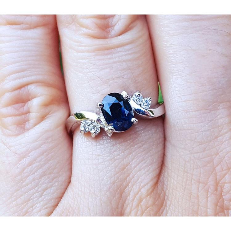 14k white gold ring with a blue oval cut sapphire on a person's finger
