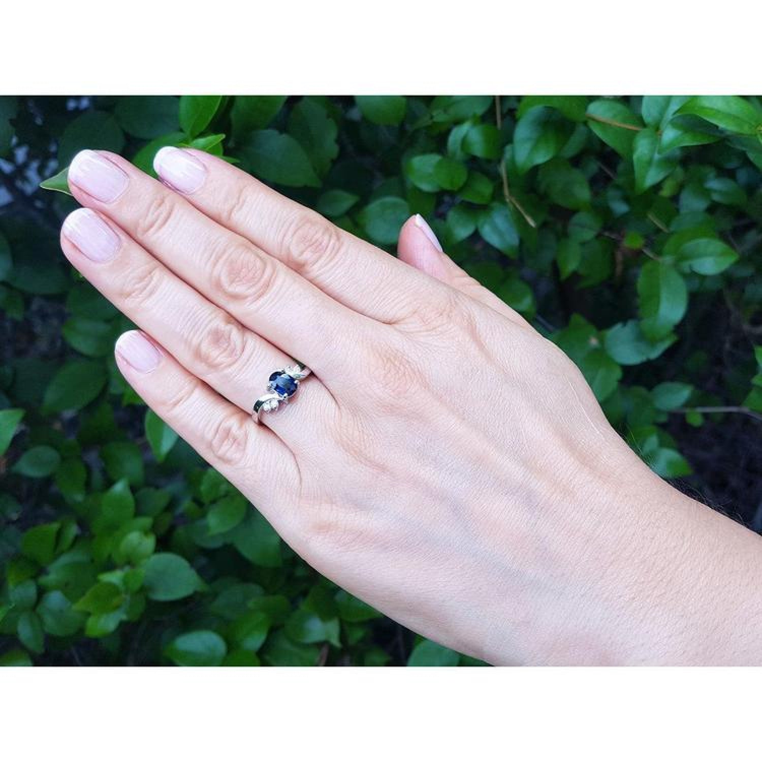 1.43 ct oval natural deep blue sapphire ring in 14K white gold with accent diamonds on a woman's hand.