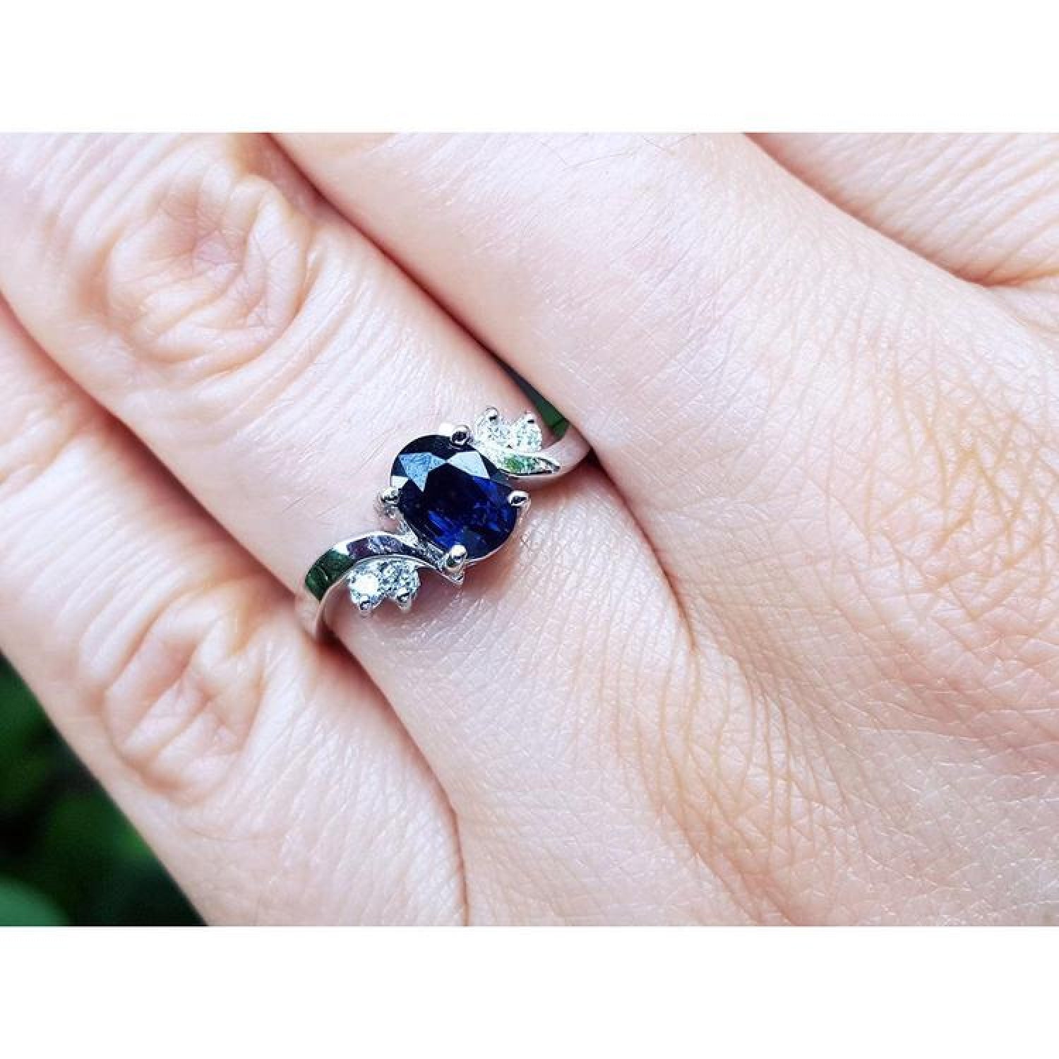 14K white gold ring with a 1.43 ct oval deep blue sapphire and accent diamonds on a hand.