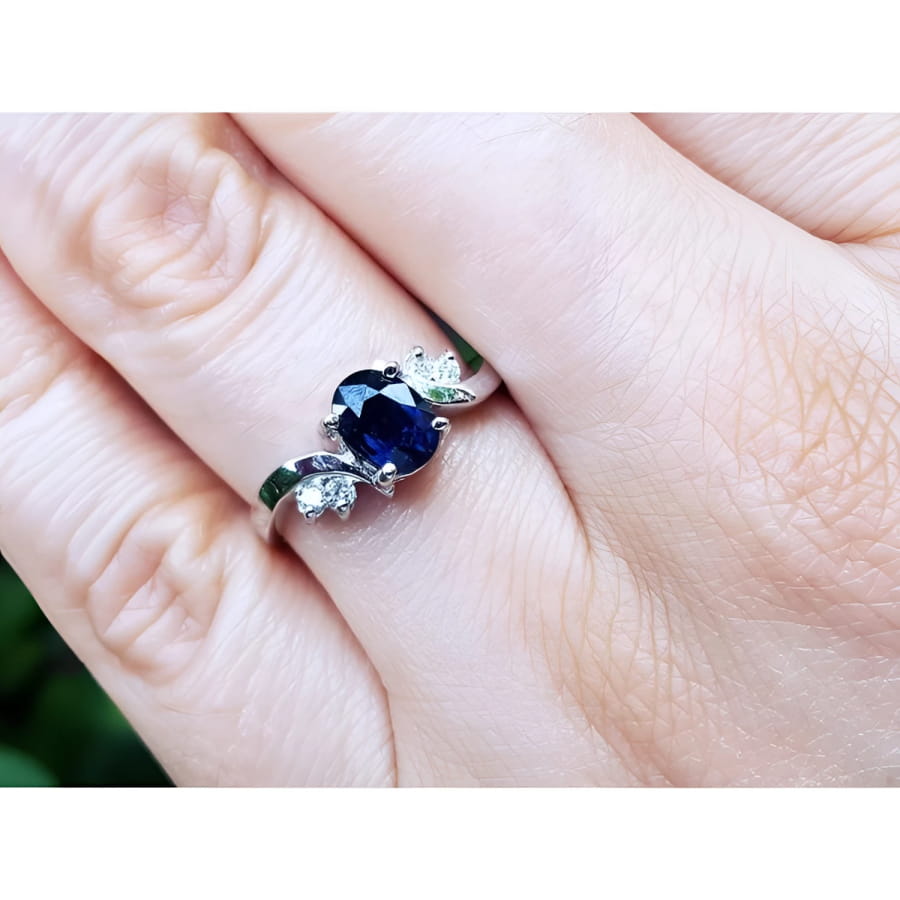 14K white gold ring with a 1.43 ct oval deep blue sapphire and accent diamonds on a hand.