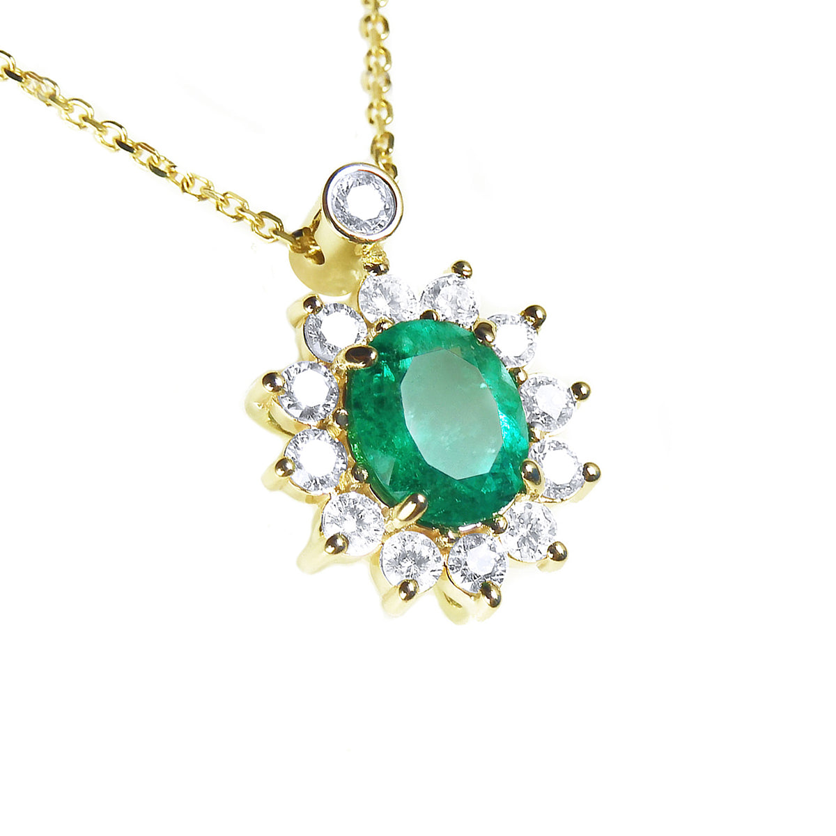 Close sight of a yellow gold necklace with a oval cut emerald gemstone in a halo diamond on a white background
