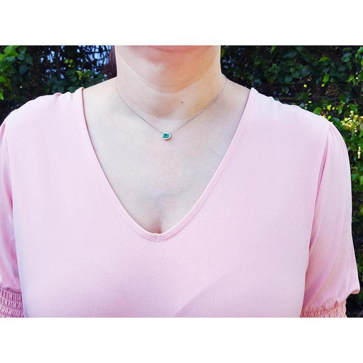 Emerald necklace with oval cut halo diamonds in 14K white gold, worn on a model.