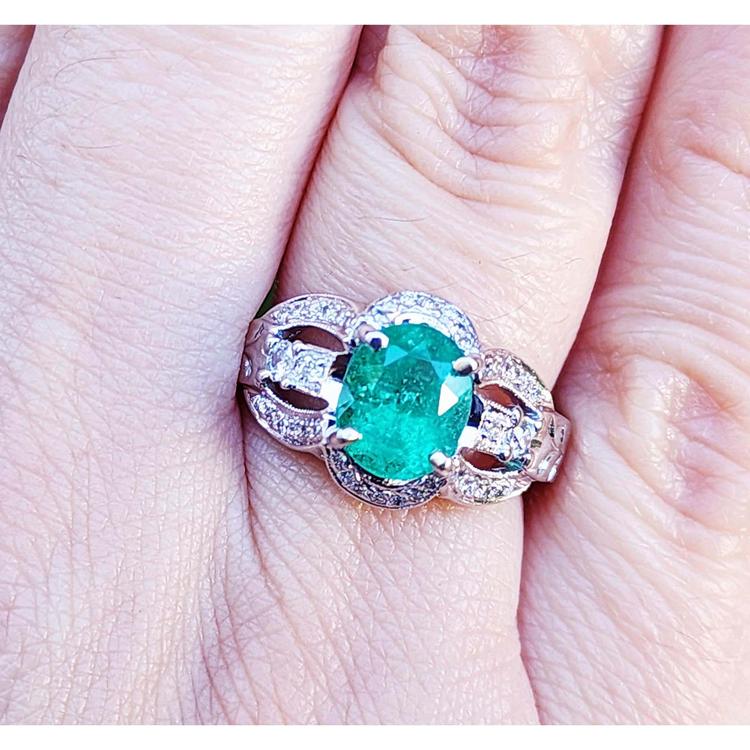 A 18k white gold oval cut colombian emerald ring with accent diamonds on a finger