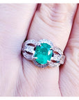 A 18k white gold oval cut colombian emerald ring with accent diamonds on a finger