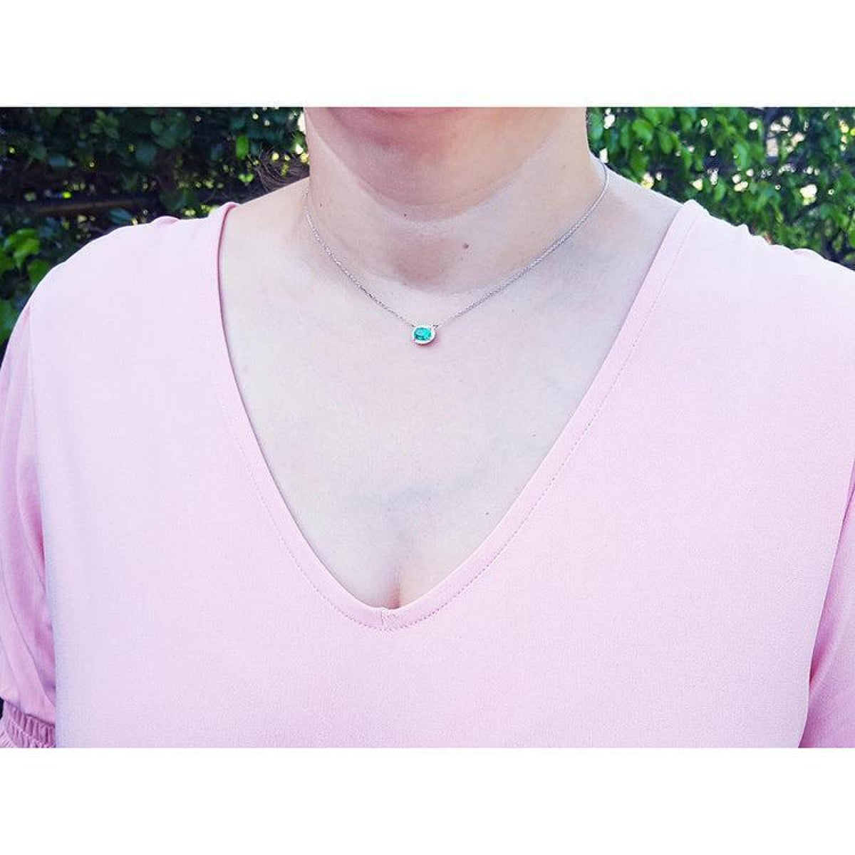 Emerald necklace with oval cut halo diamonds in 14K white gold, worn on a woman.