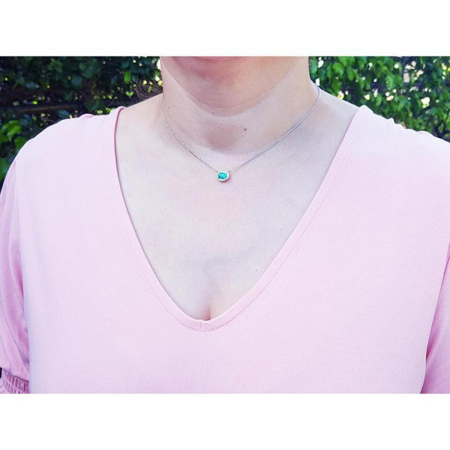 Emerald necklace with oval cut halo diamonds in 14K white gold, worn on a woman.