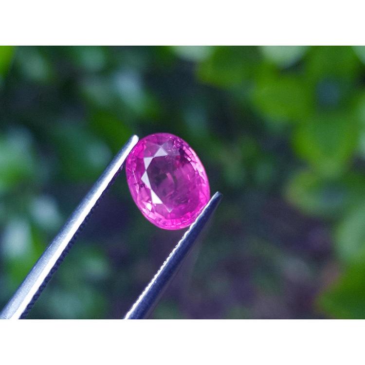 Sparkling 2.38 carat oval cut natural Mozambique ruby, held by tweezers against a green background.
