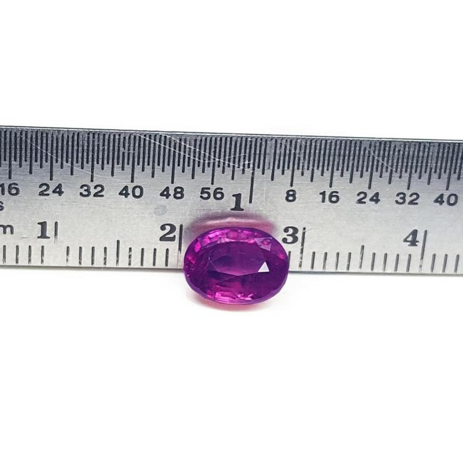 Sparkling medium rich red 2.38 carat oval cut loose natural Mozambique ruby with a ruler for scale.