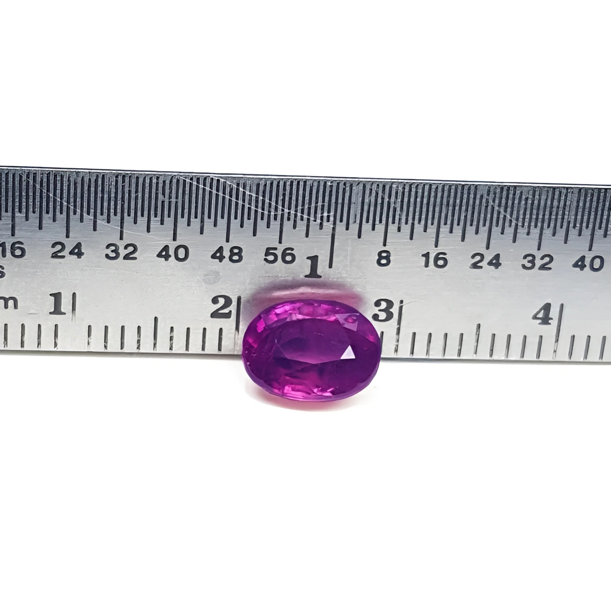 Sparkling medium rich red 2.38 carat oval cut loose natural Mozambique ruby with a ruler for scale.