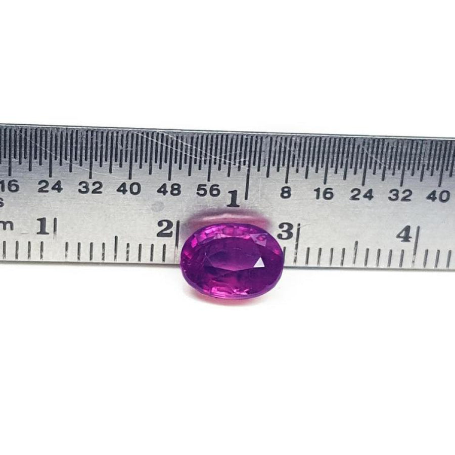 Sparkling medium rich red 2.38 carat oval cut loose natural Mozambique ruby with a ruler for scale.