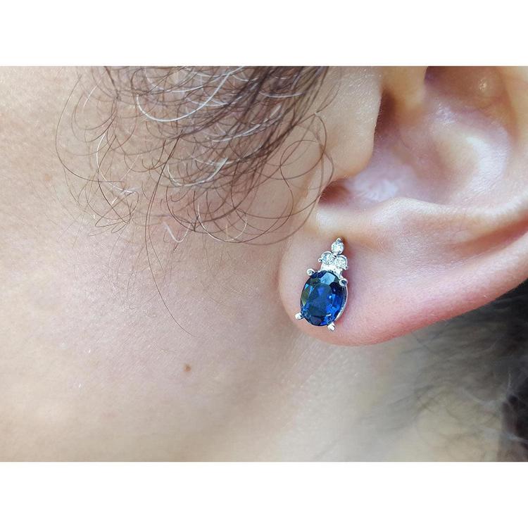 Close-up of an ear wearing a blue oval cut sapphire gemstone earring.