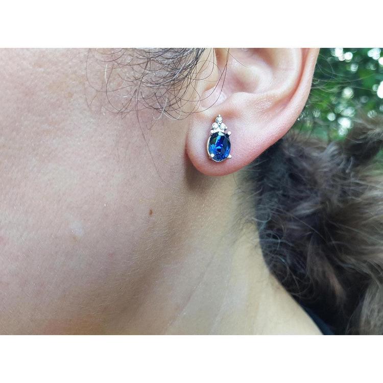 Close-up of an ear wearing a blue sapphire oval cut earring with a blurred natural background