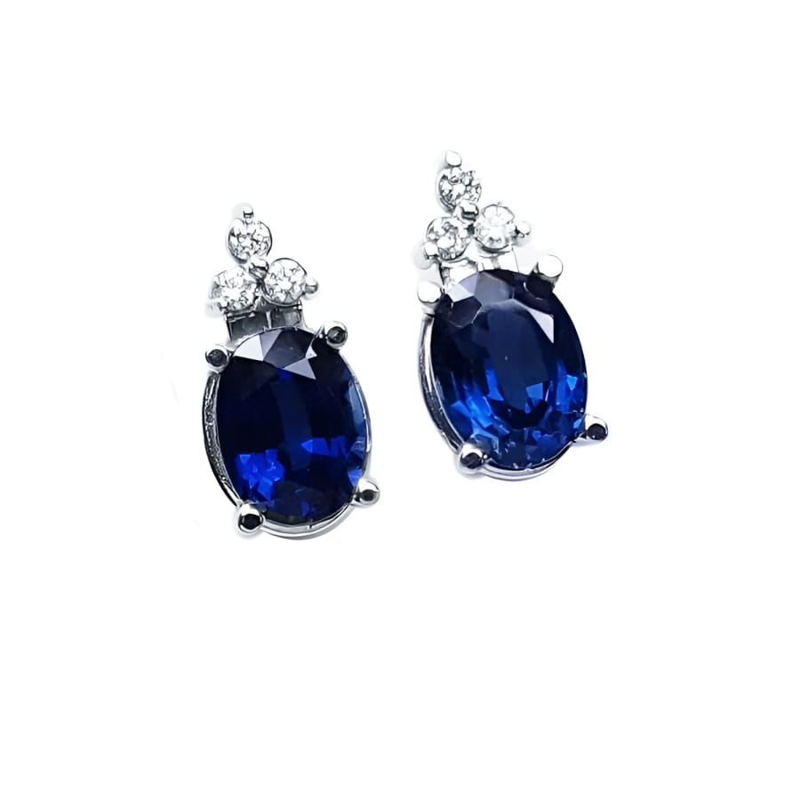 Oval deep blue sapphire stud earrings with three prong-set diamonds in 14K white gold.