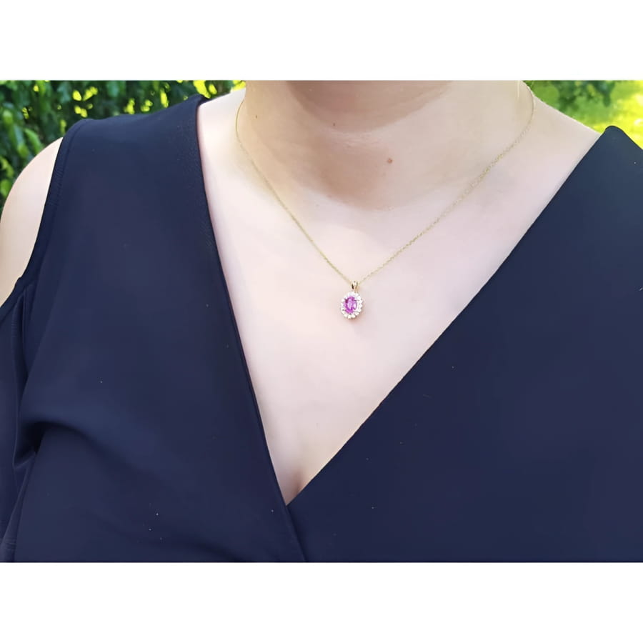 Oval pink sapphire halo diamond pendant necklace in 14K yellow gold on a model.