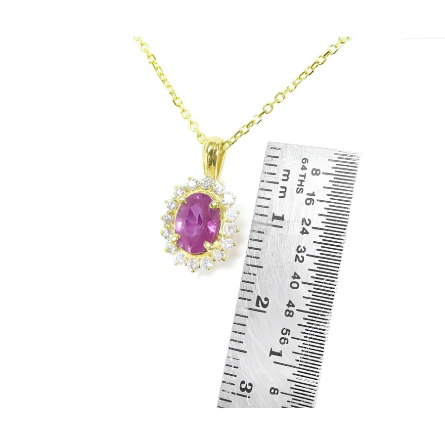 14K yellow gold necklace with oval pink sapphire halo diamond pendant, next to a ruler.