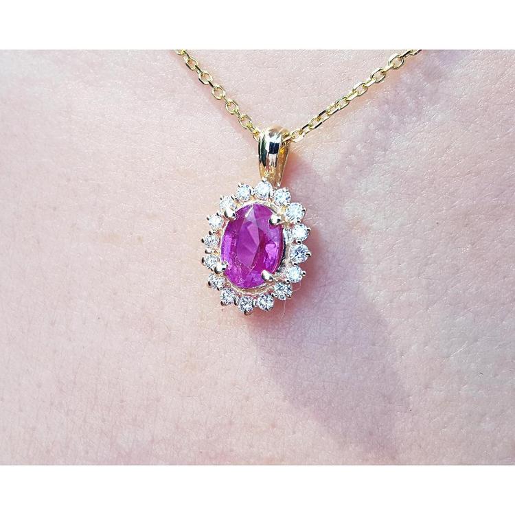 Pink oval cut sapphire gemstone halo diamond pendant with gold chain on a light skin background