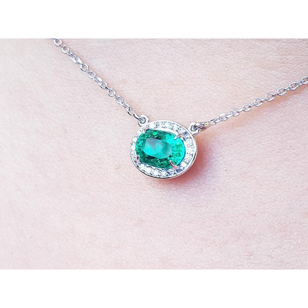 1.00 ct. oval emerald necklace with diamond halo, 14K white gold chain on skin.